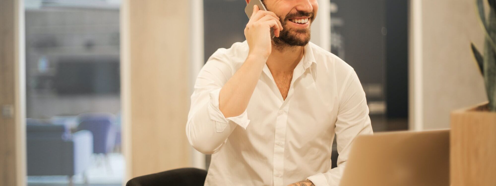 Homme d'affaires souriant au téléphone dans un bureau moderne avec un ordinateur portable et une tasse de café.