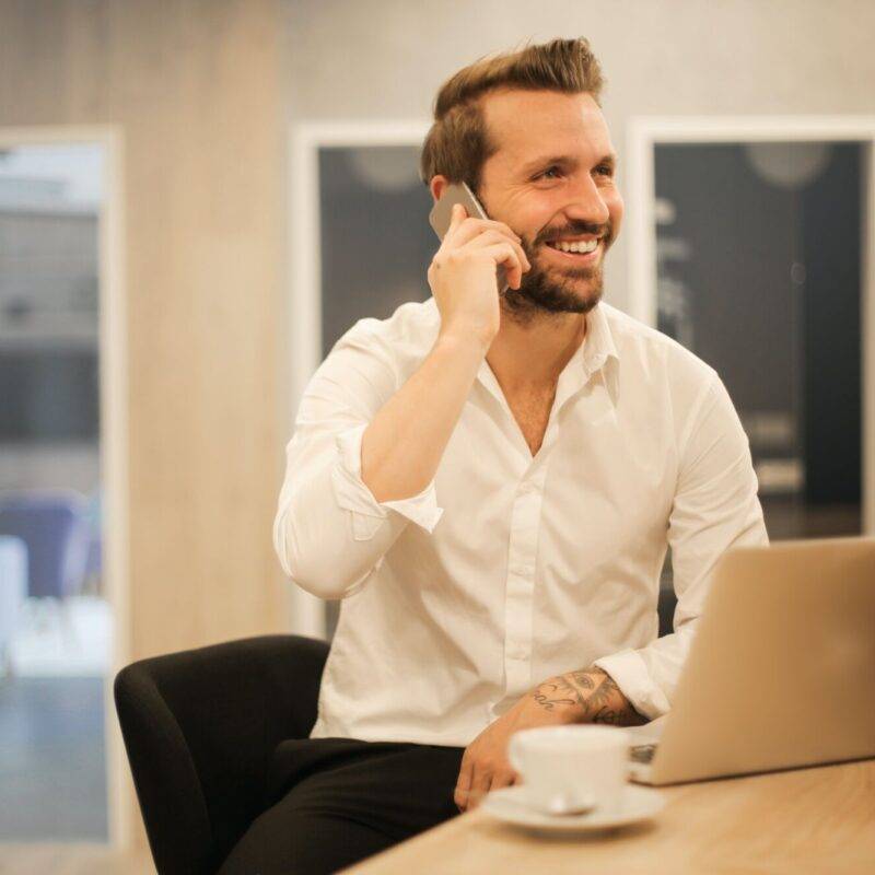 Homme d'affaires souriant au téléphone dans un bureau moderne avec un ordinateur portable et une tasse de café.
