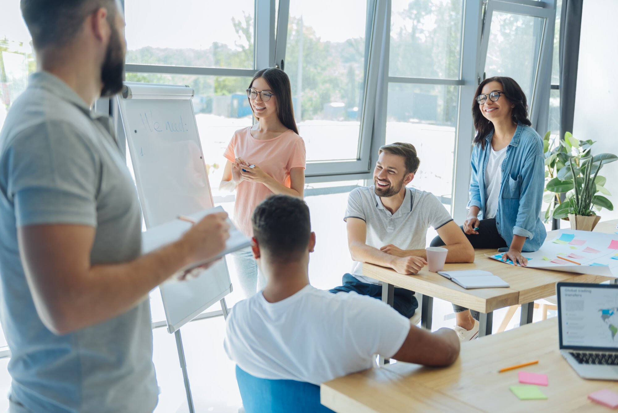ADOBESTOCK_168692897 | Cekome Groupe de collègues souriants participant à une présentation avec un tableau blanc dans un bureau lumineux.