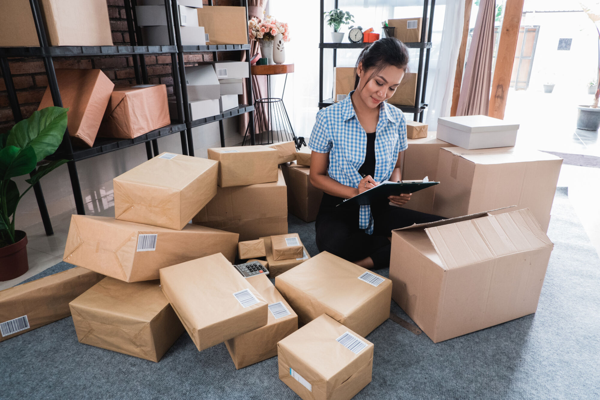 ADOBESTOCK_224520813 | Cekome Employée vérifiant l'inventaire de colis dans un entrepôt de commerce en ligne.