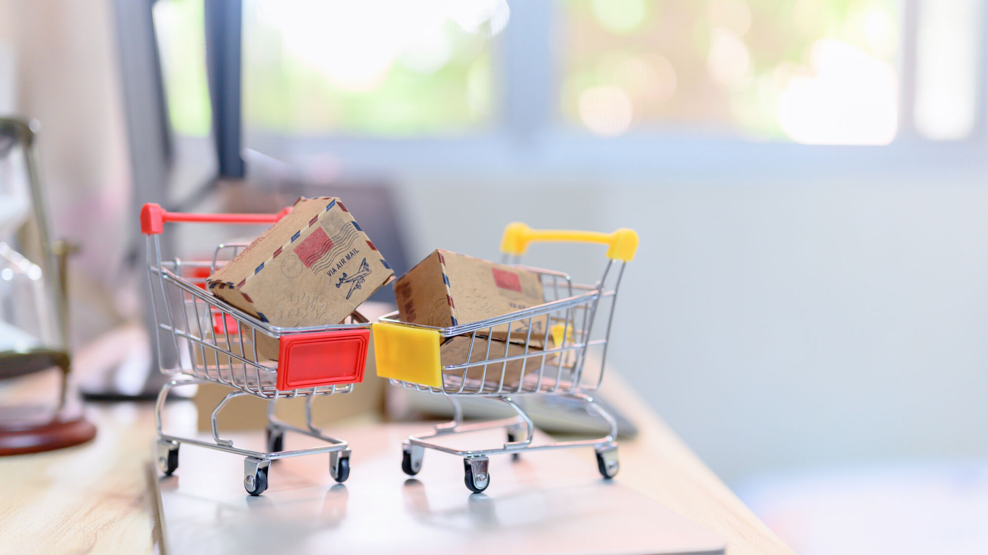 ADOBESTOCK_348424945 | Cekome Mini caddie de supermarché contenant des paquets sur un bureau, symbolisant les achats en ligne.