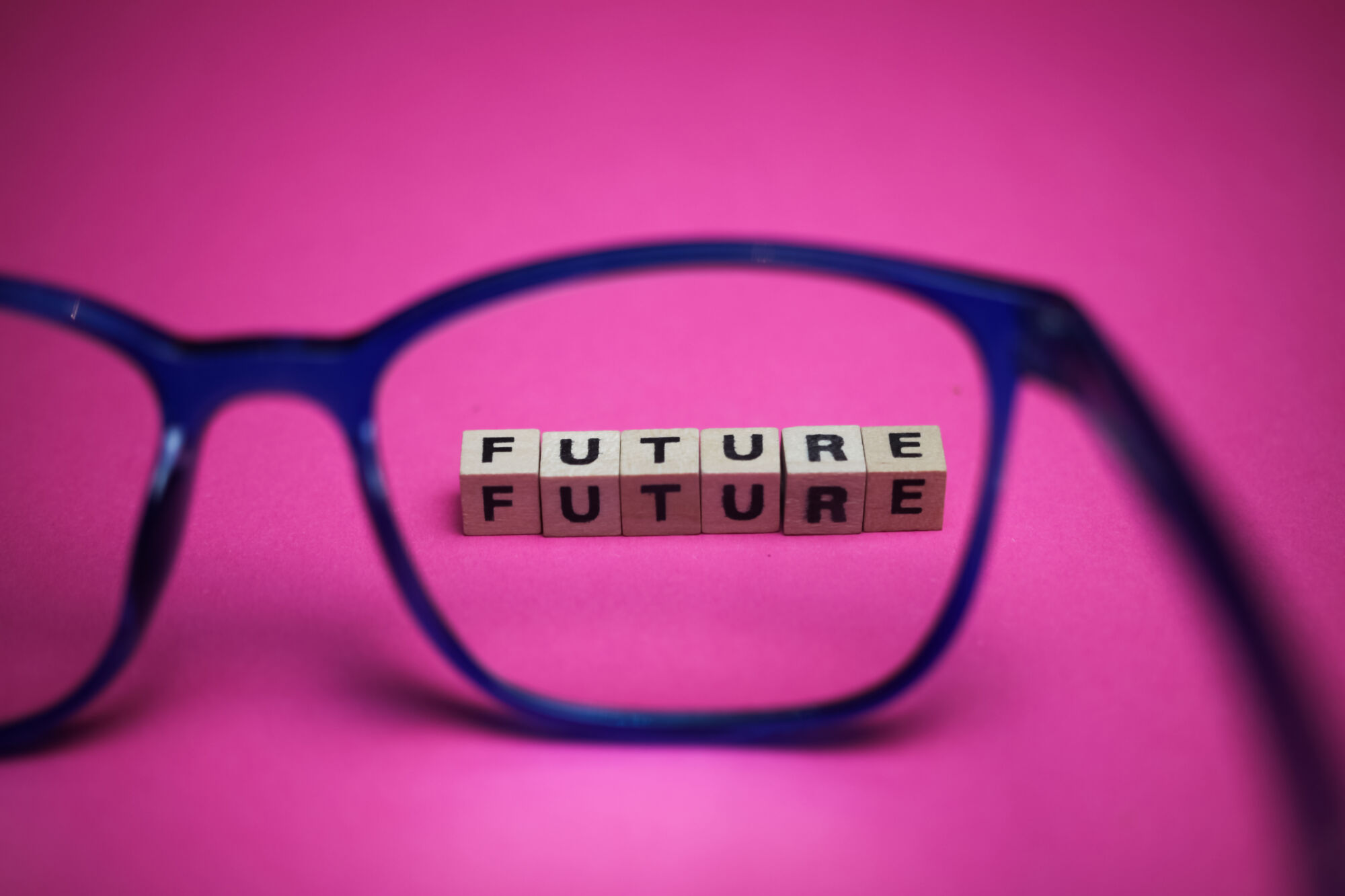 ADOBESTOCK_380030139 | Cekome Lunettes bleues mettant en évidence des cubes en bois formant le mot 'FUTURE' sur un fond rose.