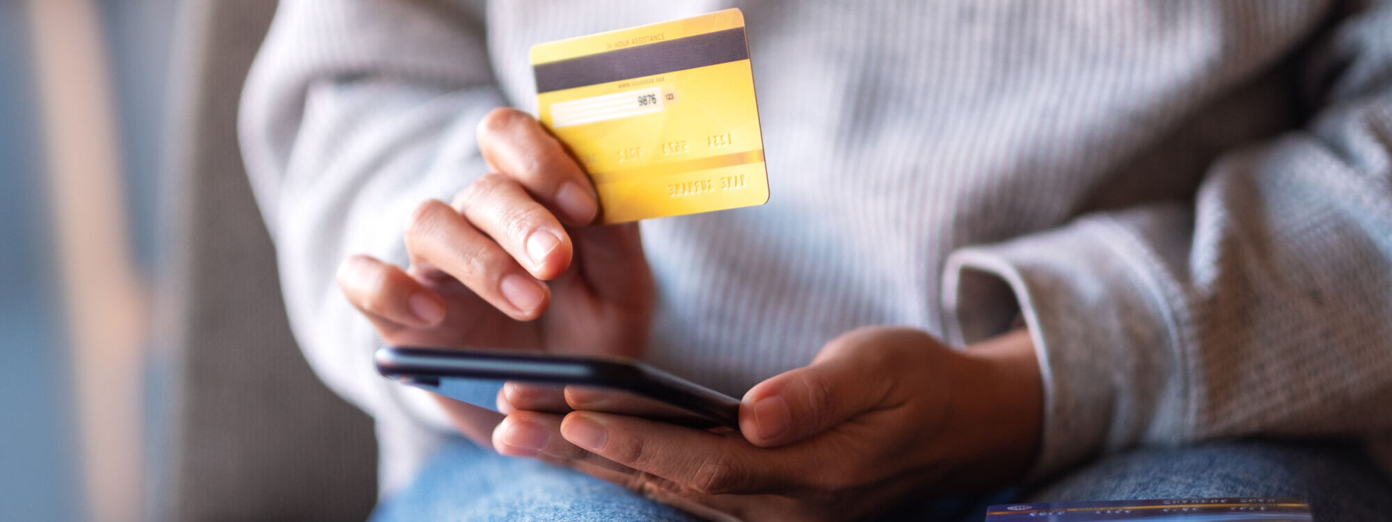Gros plan sur des mains tenant une carte de cr&eacute;dit et un smartphone pour un paiement en ligne.