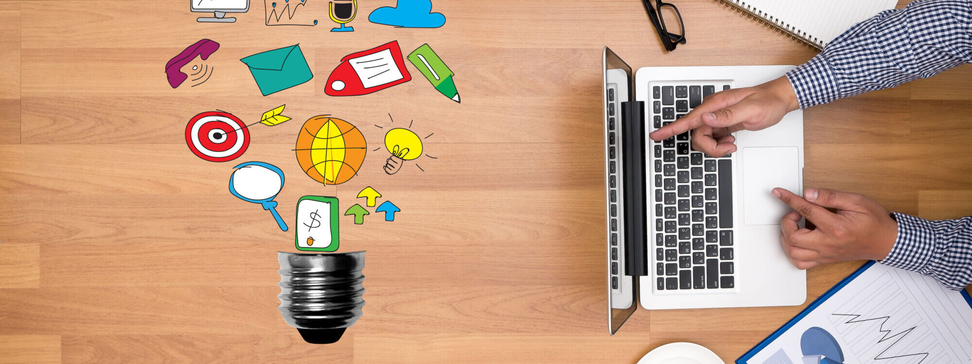 Main d'une personne travaillant sur un ordinateur avec des ic&ocirc;nes de contenu num&eacute;rique s'envolant d'une ampoule.