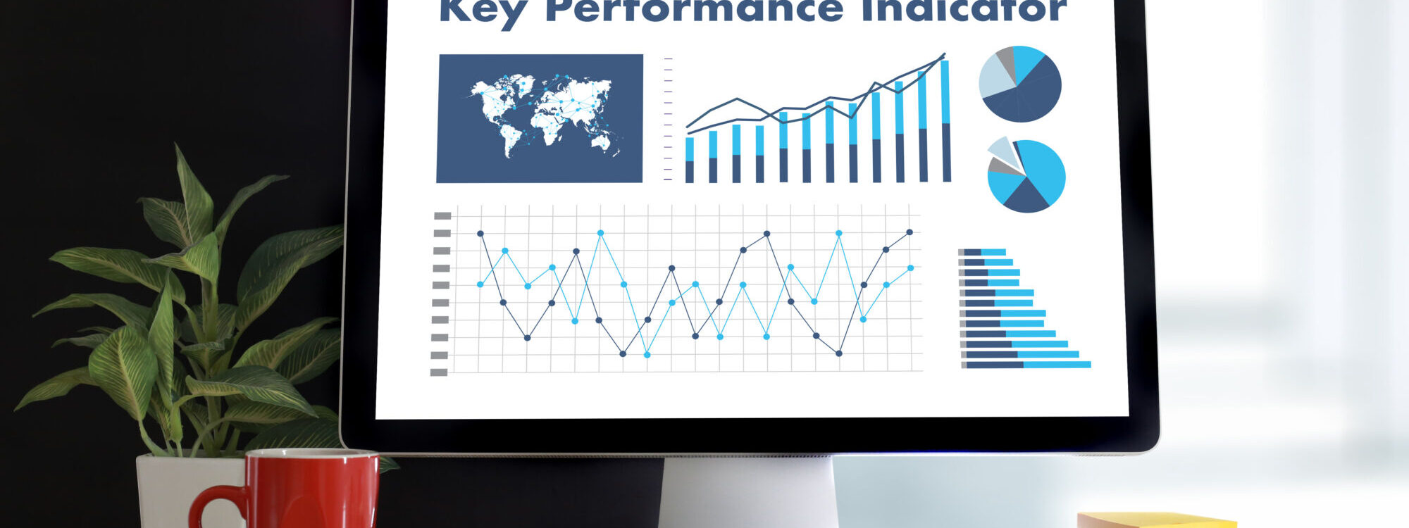 &Eacute;cran d'ordinateur montrant des graphiques et des donn&eacute;es pour les indicateurs de performance cl&eacute;s (KPI) avec une plante et une tasse rouge sur le bureau.