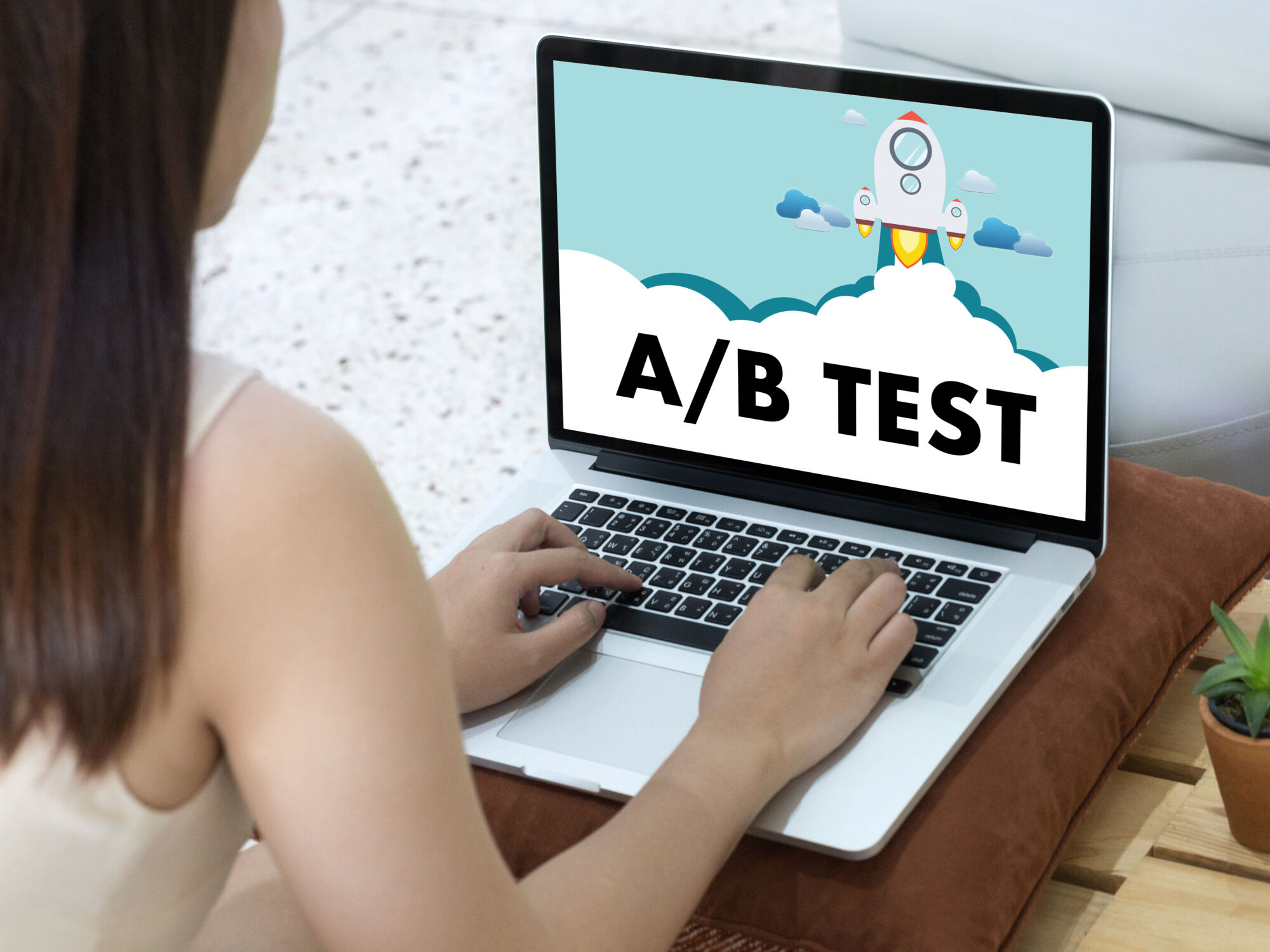 ADOBESTOCK_173416575 | Cekome Femme travaillant sur un ordinateur portable affichant une illustration d'un test A/B avec une fusée décollant à travers les nuages.