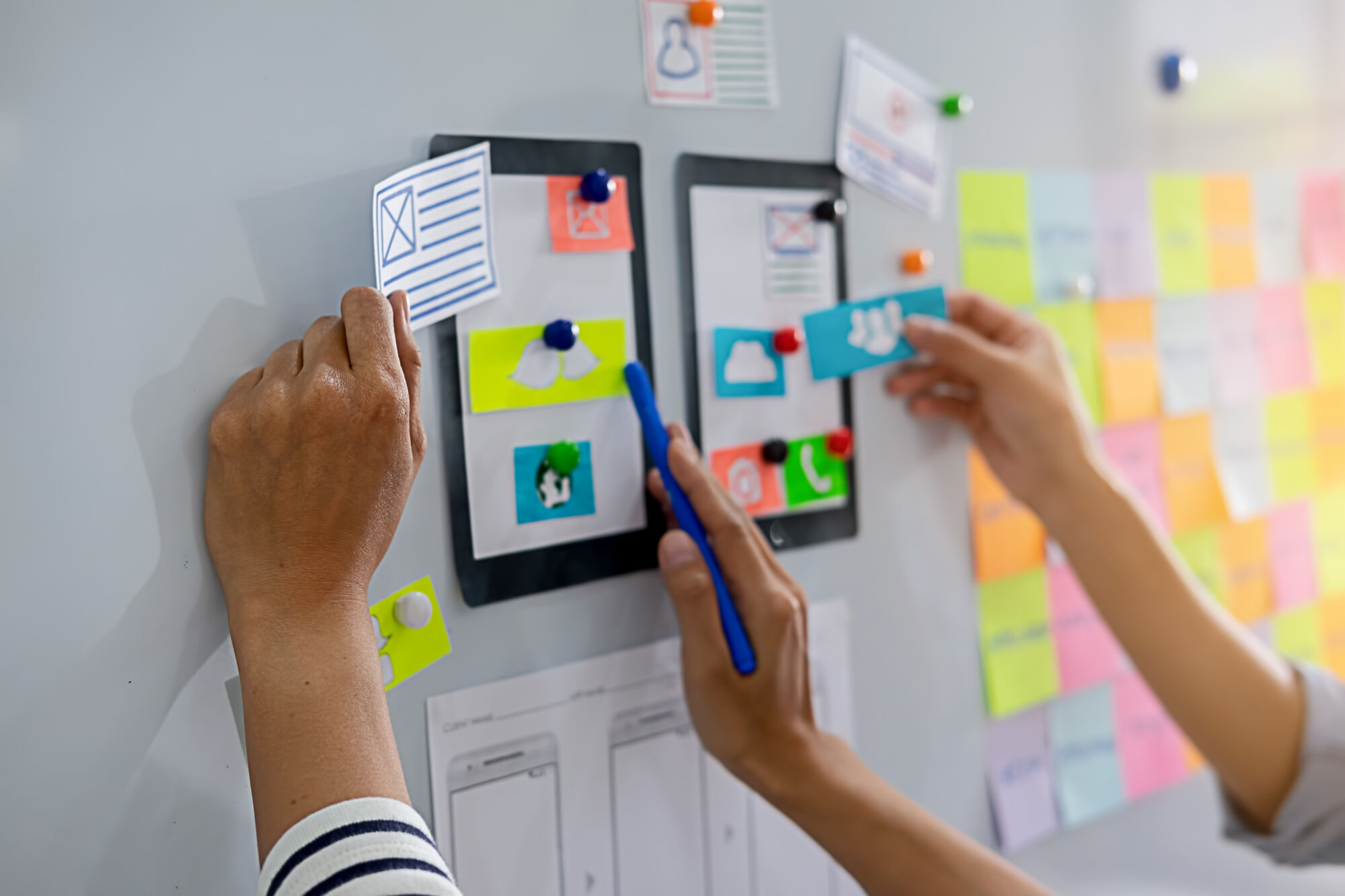 ADOBESTOCK_217151835 | Cekome Mains plaçant des notes adhésives et des icônes sur un tableau blanc lors d'une séance de brainstorming pour le développement d'applications.
