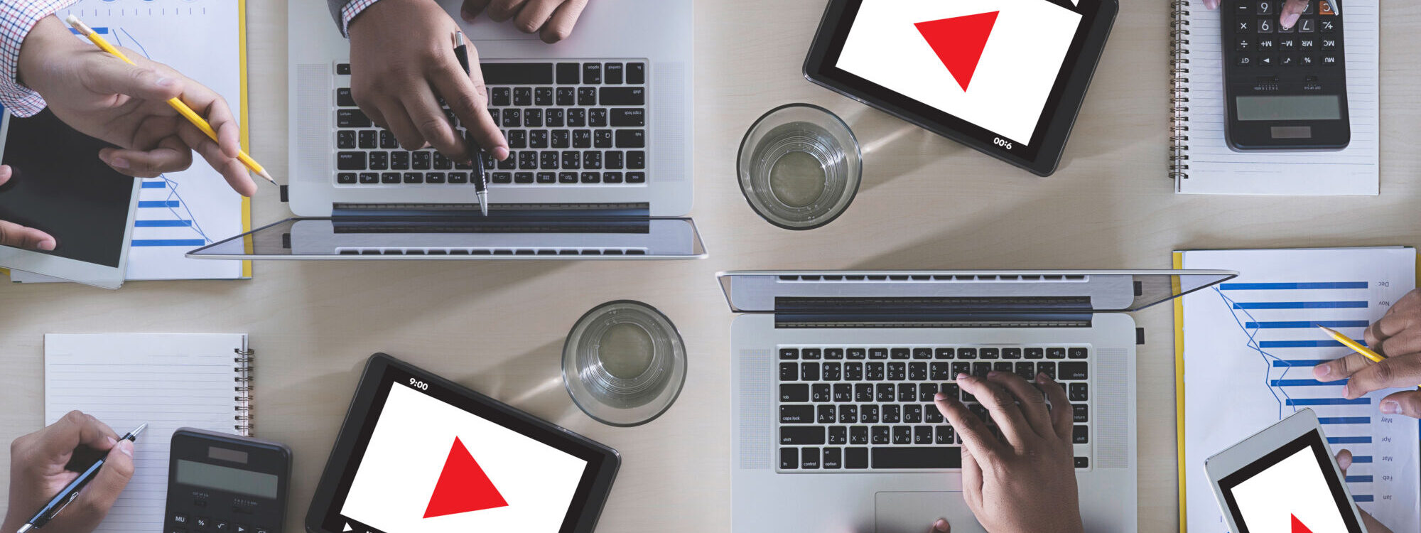 Vue de dessus d'une r&eacute;union d'&eacute;quipe avec des ordinateurs portables et des tablettes affichant des graphiques rouges triangulaires.