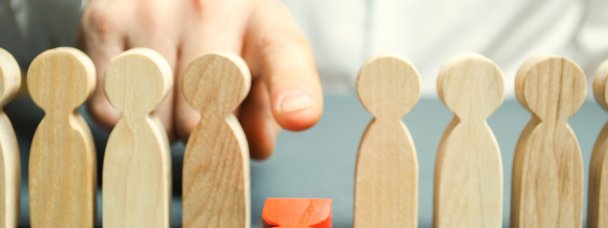 Main sélectionnant une figure unique en rouge parmi un groupe de figurines en bois, concept de leadership ou de recrutement.