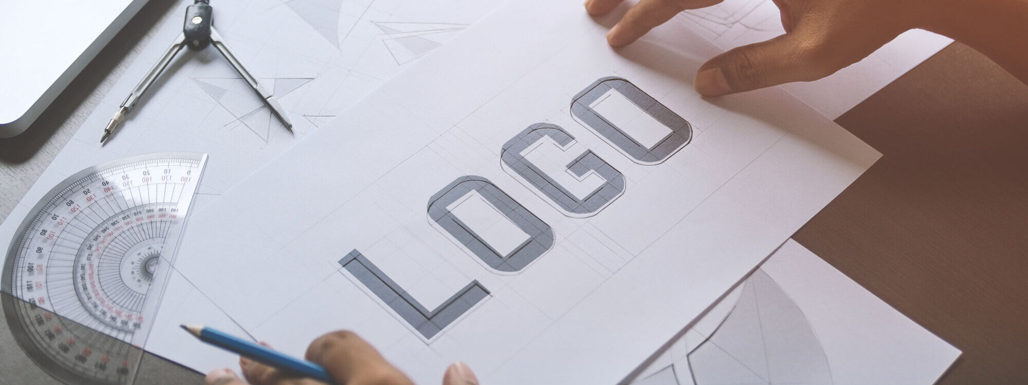 ADOBESTOCK_271407946 2000X750 | Cekome Mains travaillant sur un dessin de concept de logo avec outils de dessin technique.