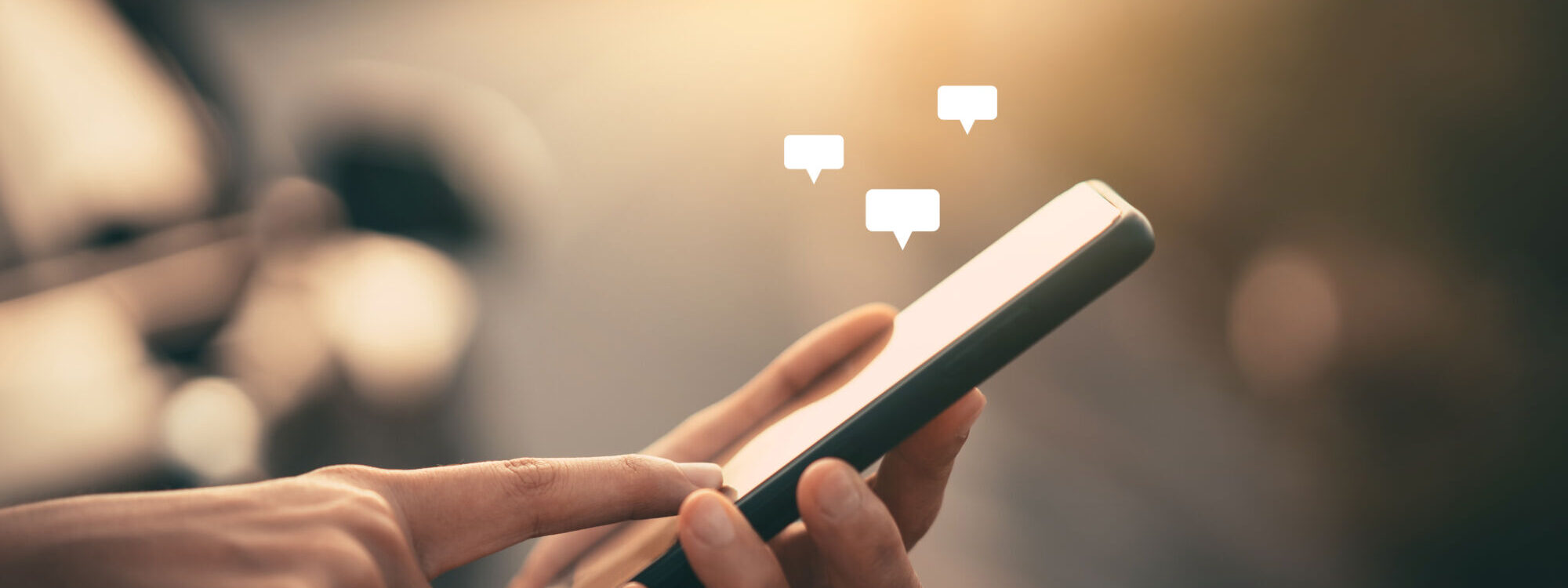 Main tenant un smartphone avec des ic&ocirc;nes de bulles de chat, symbolisant la communication ou les r&eacute;seaux sociaux.