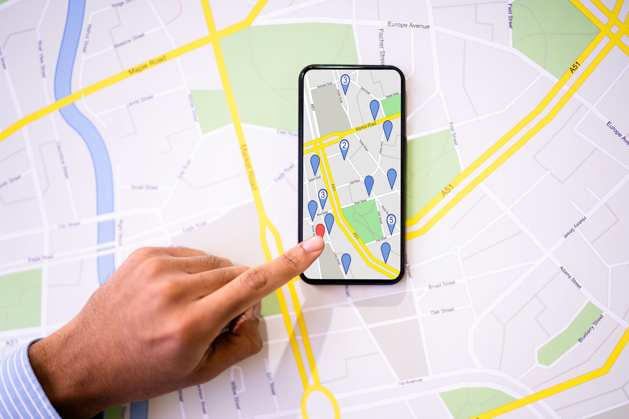 ADOBESTOCK_481731939 | Cekome Doigt pointant sur une carte interactive sur un smartphone avec des icônes de localisation et un plan de ville en arrière-plan.