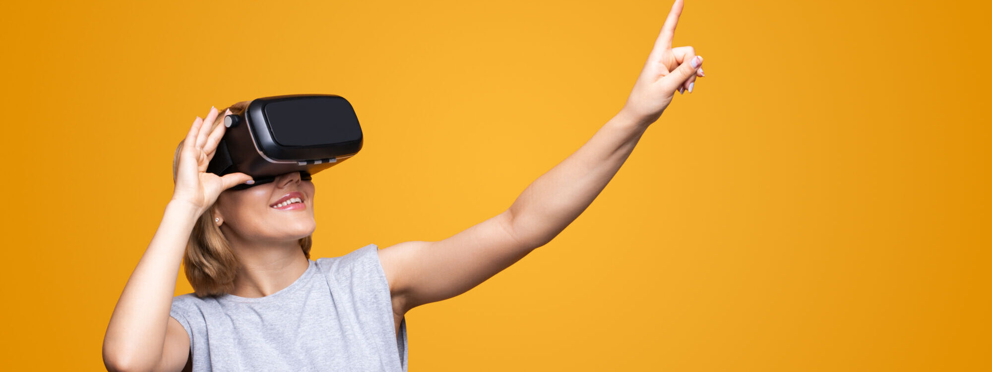Femme souriante utilisant un casque de r&eacute;alit&eacute; virtuelle pointant vers un espace vide sur fond orange