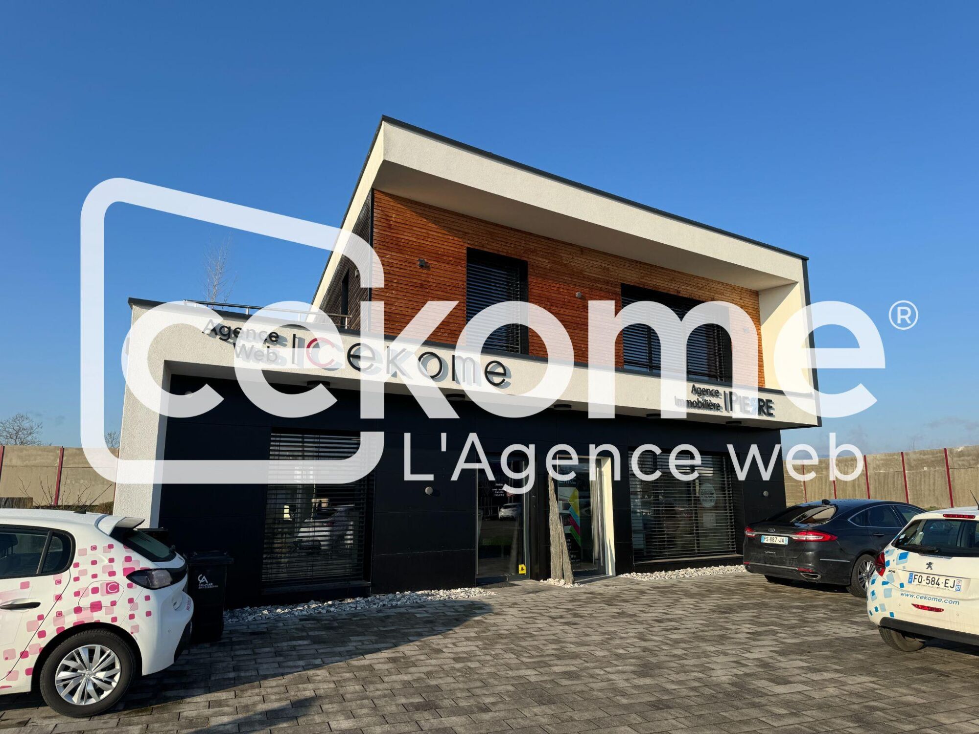 Fa&ccedil;ade moderne d'un b&acirc;timent de bureau avec enseigne de Cekome et v&eacute;hicules gar&eacute;s.