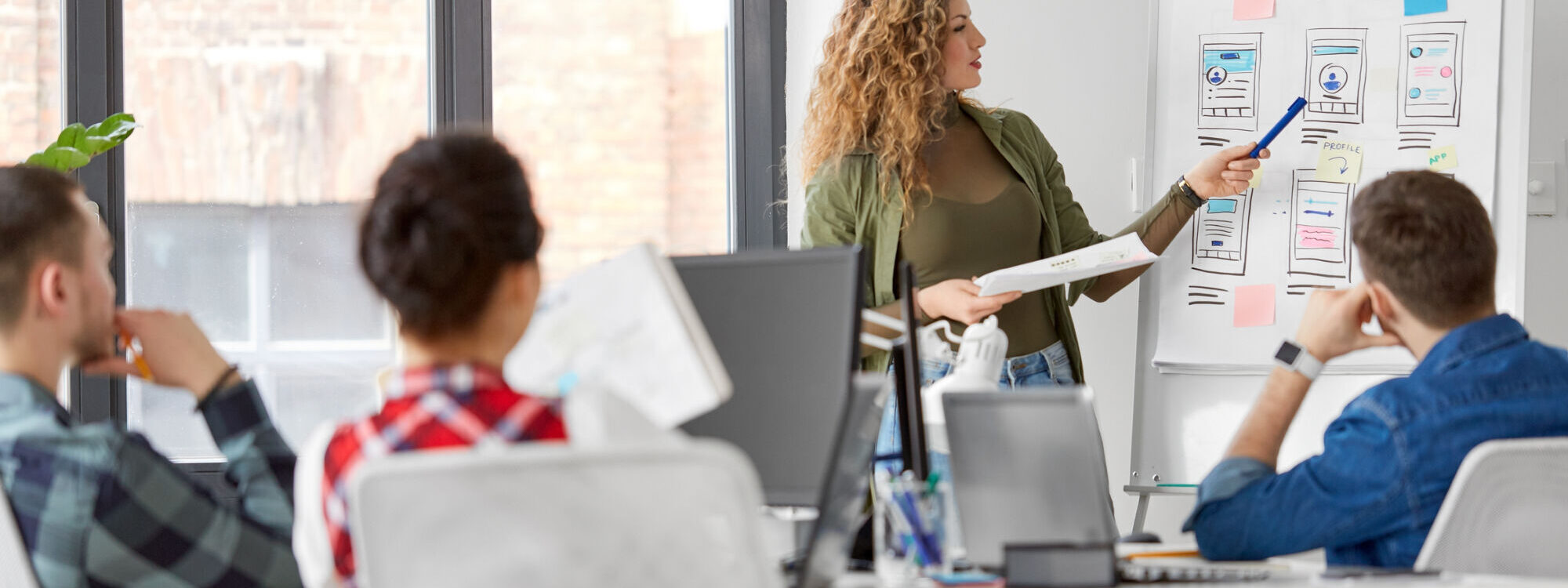 Photo d'une femme présentant des maquettes d'interface utilisateur lors d'une réunion d'équipe en bureau.