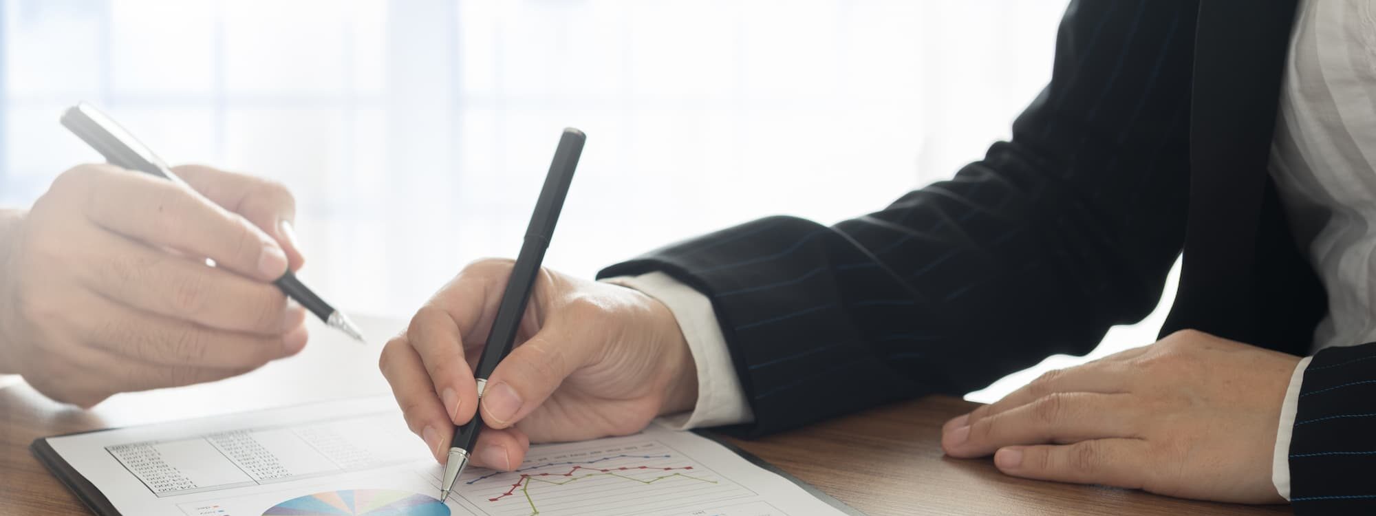 Deux coll&egrave;gues analysant des donn&eacute;es financi&egrave;res sur des documents avec diagrammes circulaires.