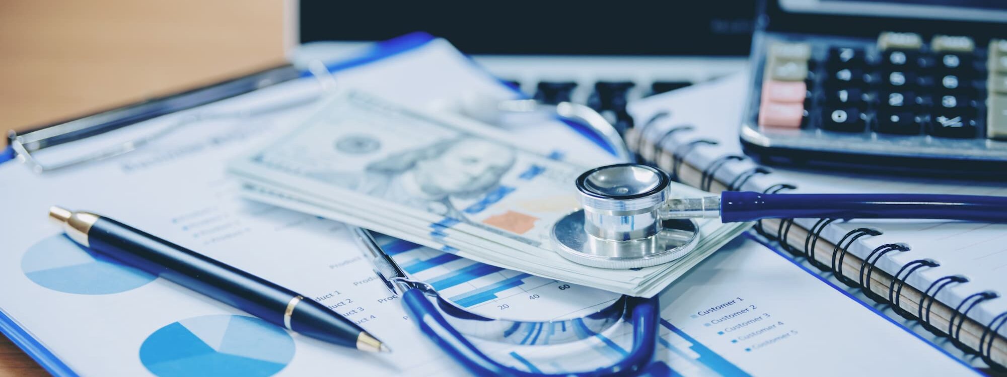 St&eacute;thoscope et billets de banque sur des documents financiers avec graphiques et calculatrice en arri&egrave;re-plan.