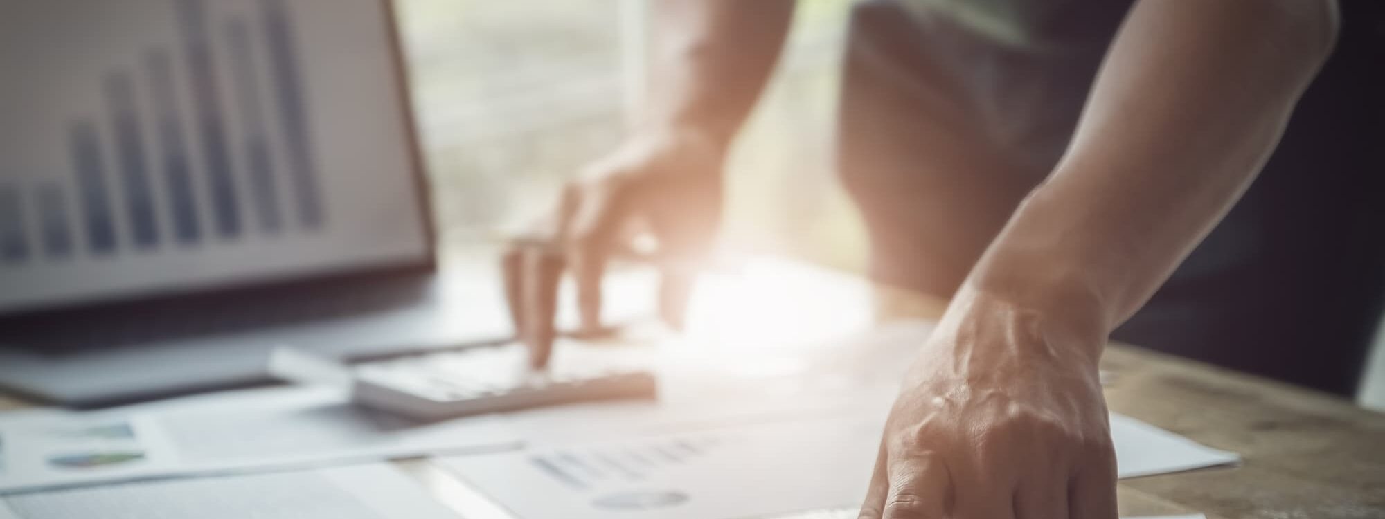 Main pointant vers des graphiques financiers sur des documents avec ordinateur portable flou en arri&egrave;re-plan.