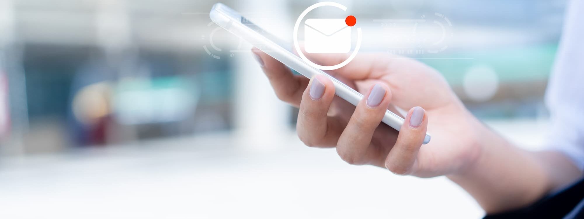 ADOBESTOCK_303402022 2000X750 | Cekome Main tenant un smartphone avec notification d'email sur fond urbain flouté.