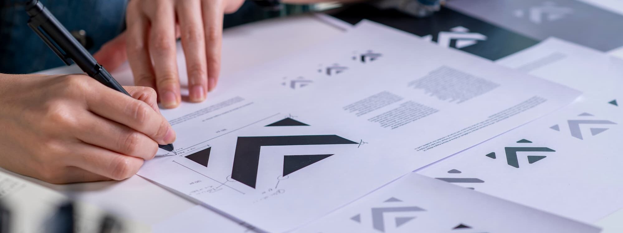 Personne analysant des prototypes de logos avec des formes g&eacute;om&eacute;triques sur documents papier