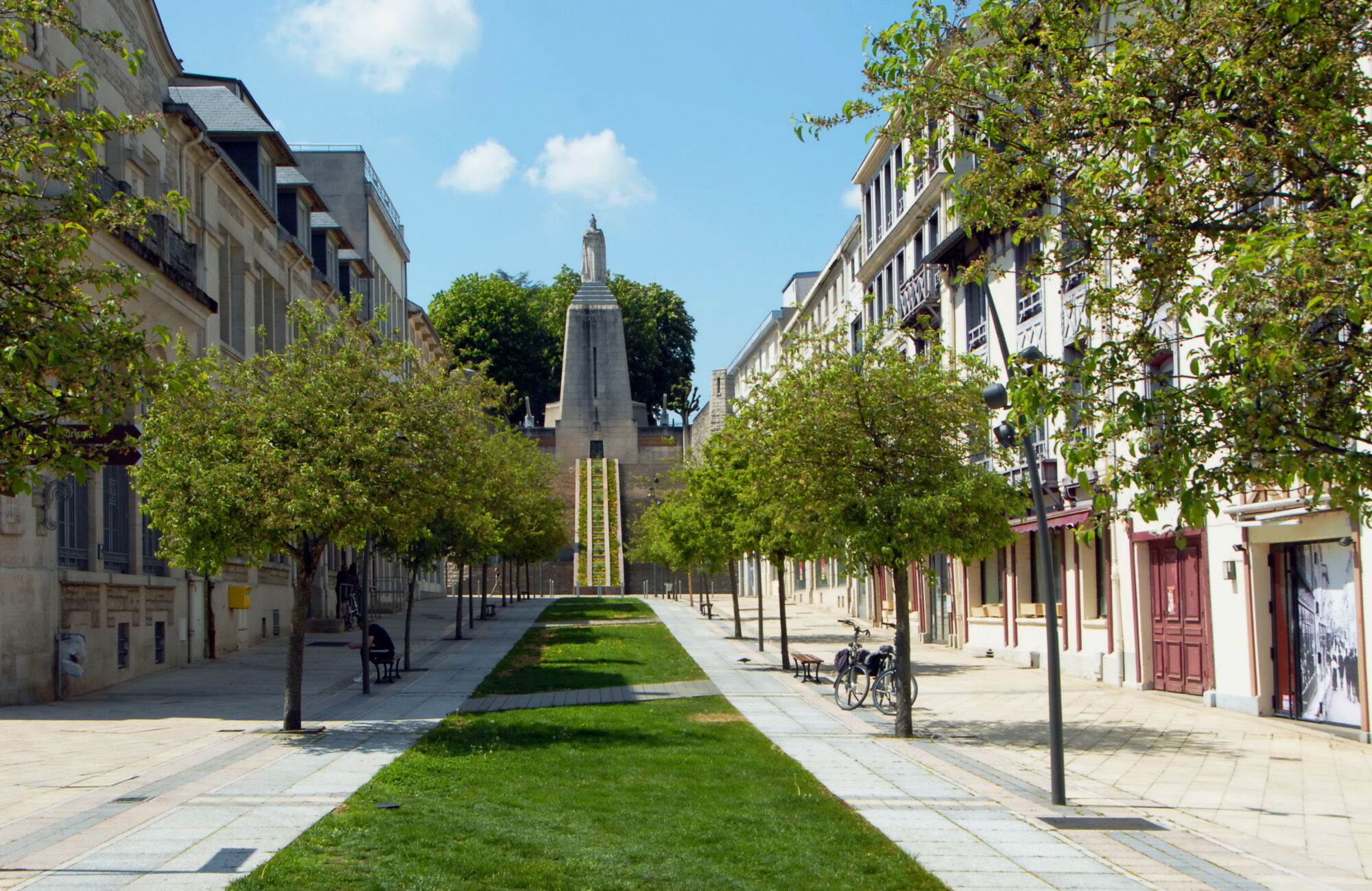 All&eacute;e pi&eacute;tonne bord&eacute;e d'arbres menant &agrave; un monument comm&eacute;moratif en ville.