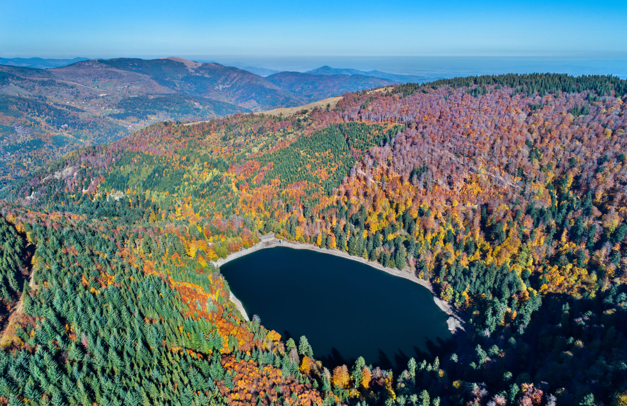 Vue a&eacute;rienne d'un lac de montagne entour&eacute; de for&ecirc;ts aux couleurs d'automne.