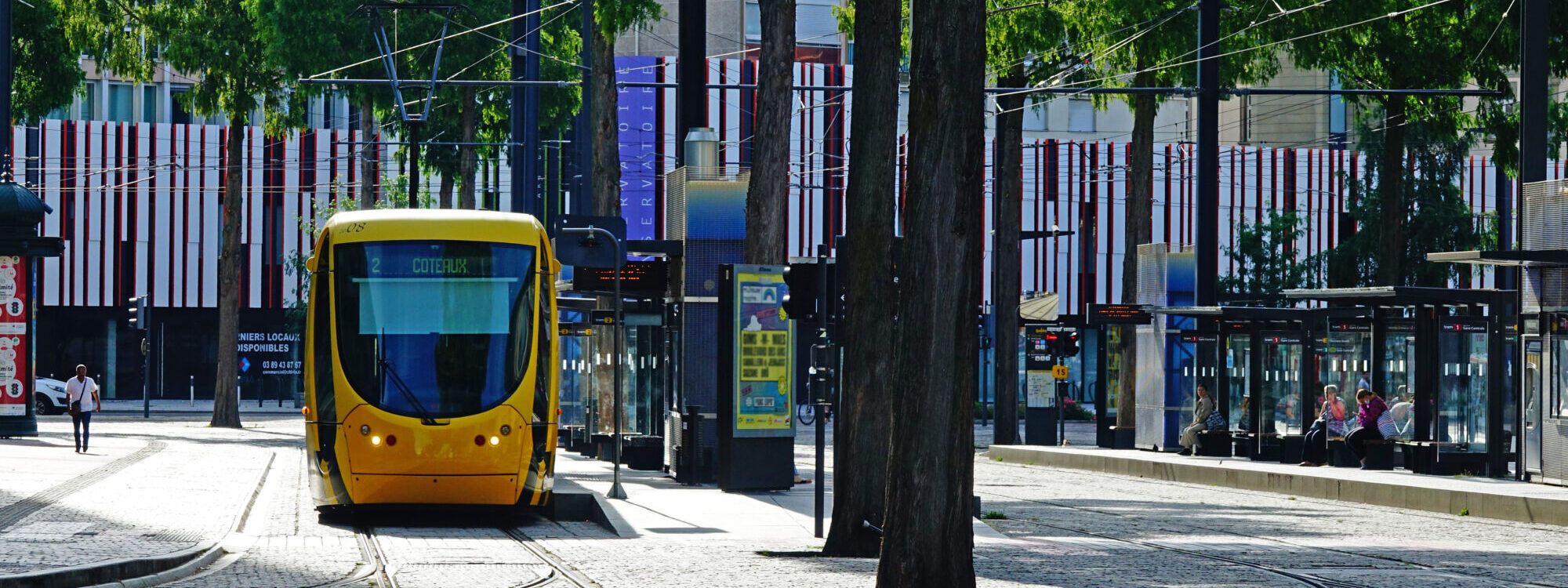 Tramway jaune dans une rue bord&eacute;e d'arbres avec station de tramway moderne.