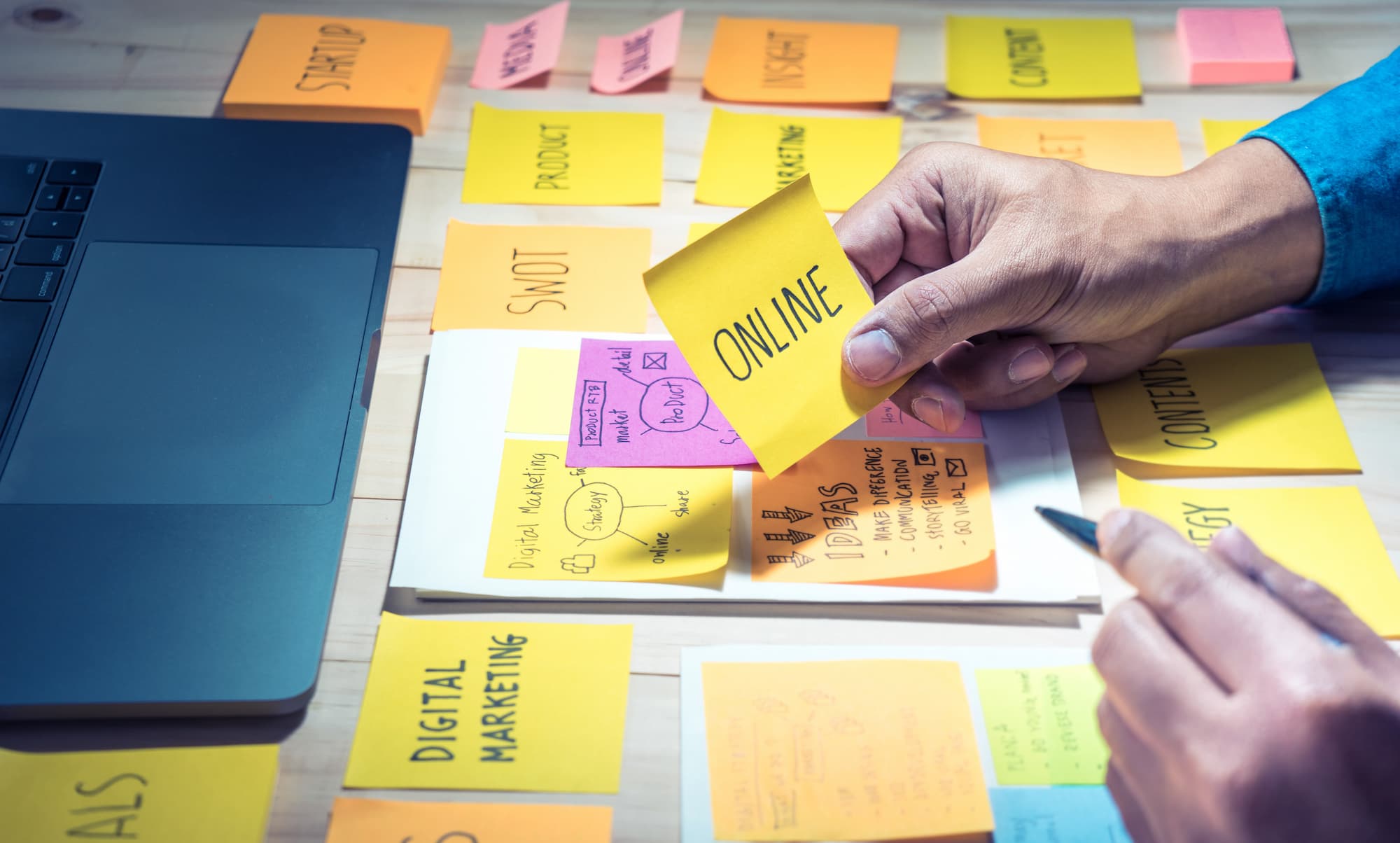 ADOBESTOCK_162500071 | Cekome Main plaçant des post-its sur un bureau avec des plans de stratégie de contenu et marketing numérique.