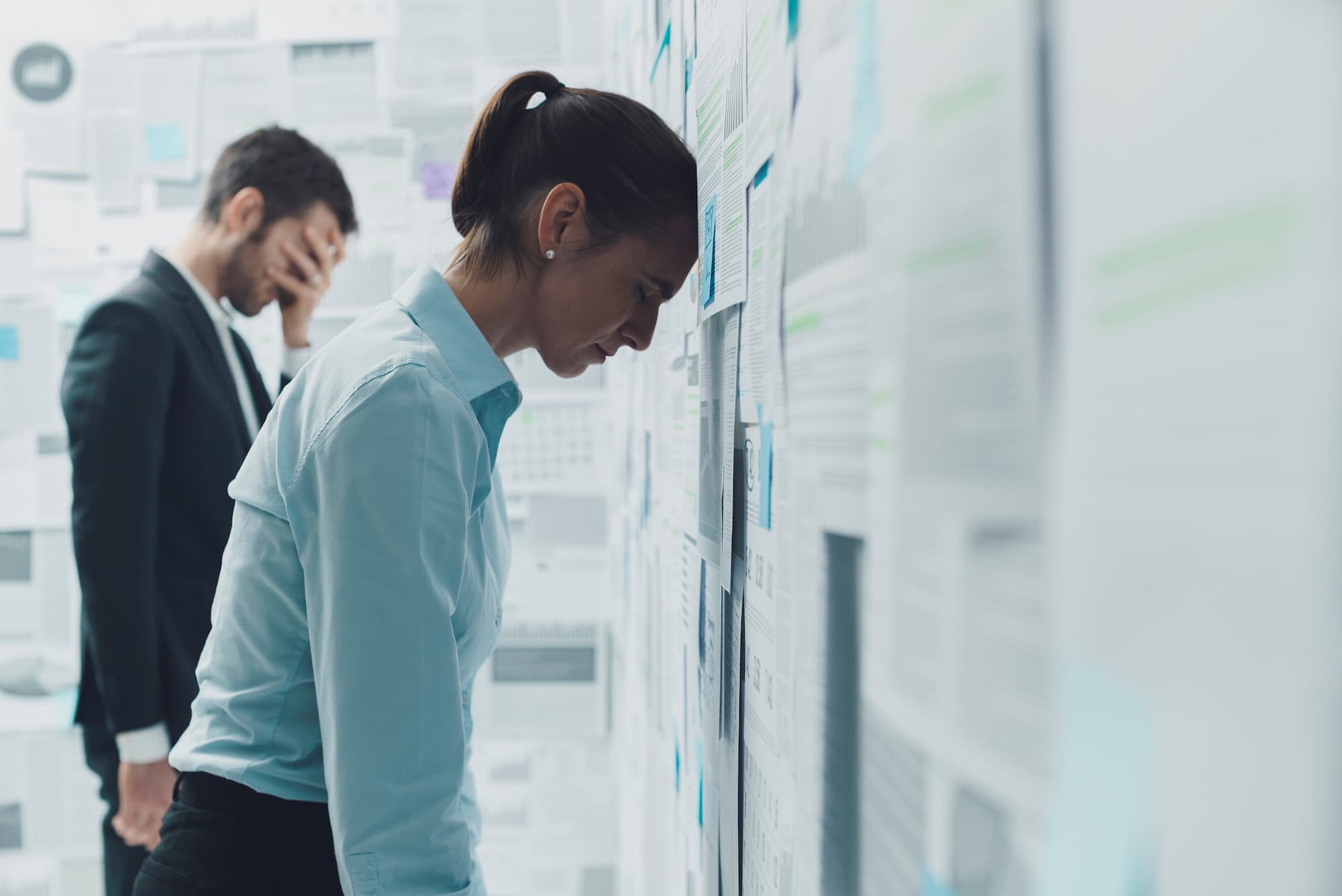 ADOBESTOCK_302302192 | Cekome Deux collègues devant un mur rempli de documents, l'un d'eux semble stressé et l'autre découragé