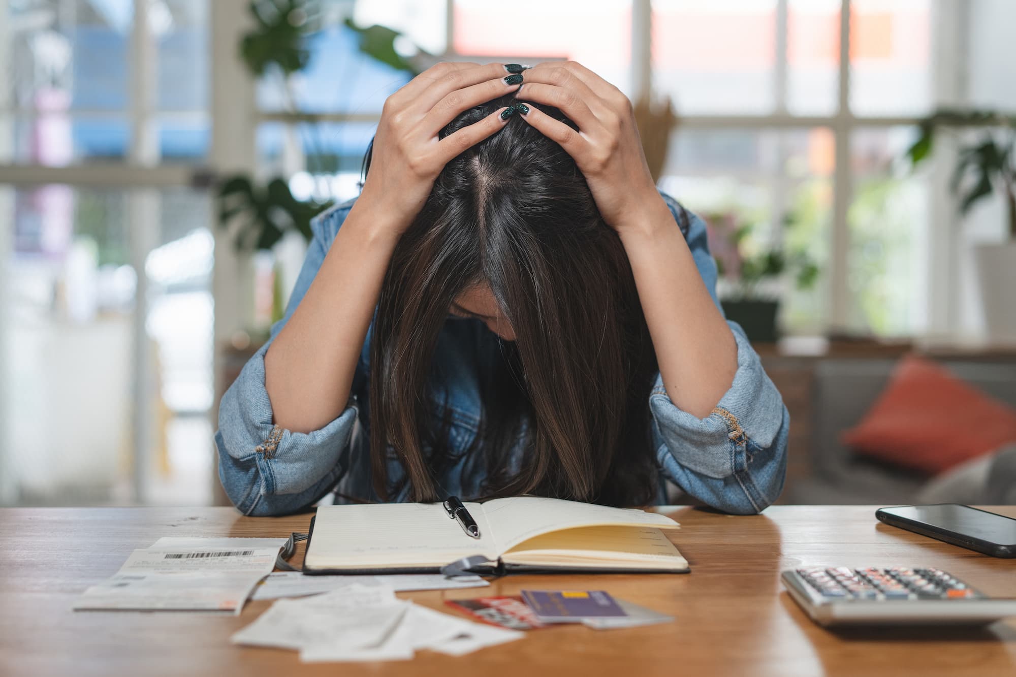 ADOBESTOCK_313442117 | Cekome Jeune femme stressée tenant sa tête en regardant des papiers et un ordinateur portable sur une table en bois dans un environnement lumineux