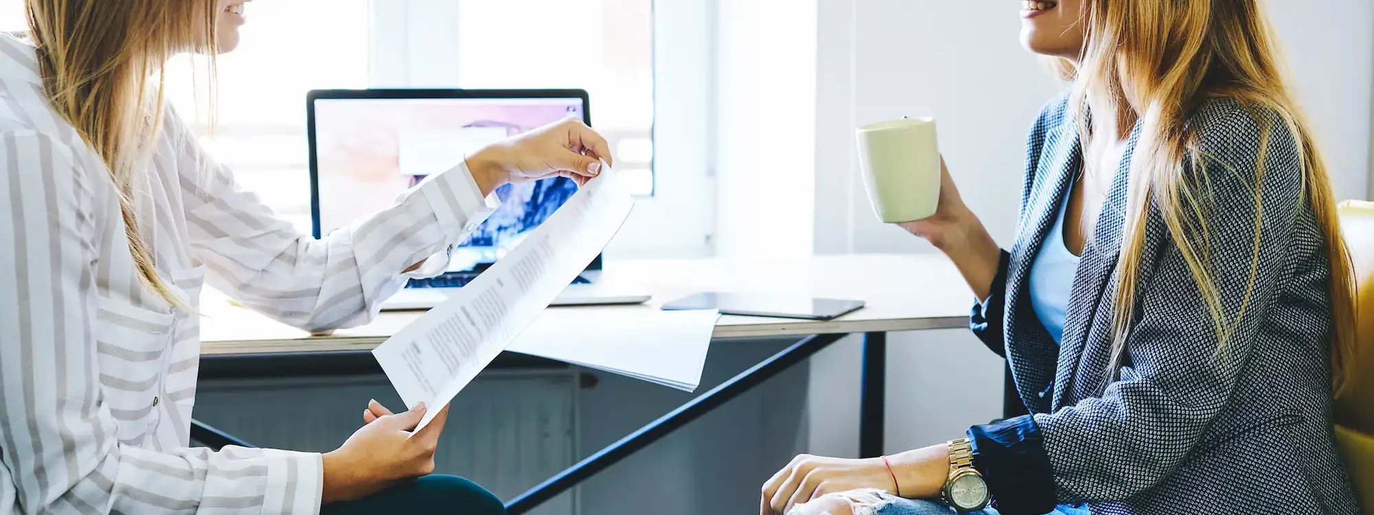 Deux femmes discutant de recrutement dans un bureau, l'une tenant un document et l'autre une tasse de café