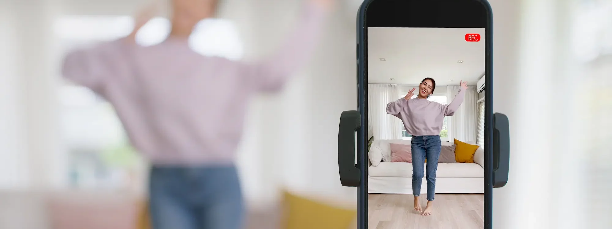 Femme dansant devant un smartphone en mode enregistrement vidéo dans un salon lumineux