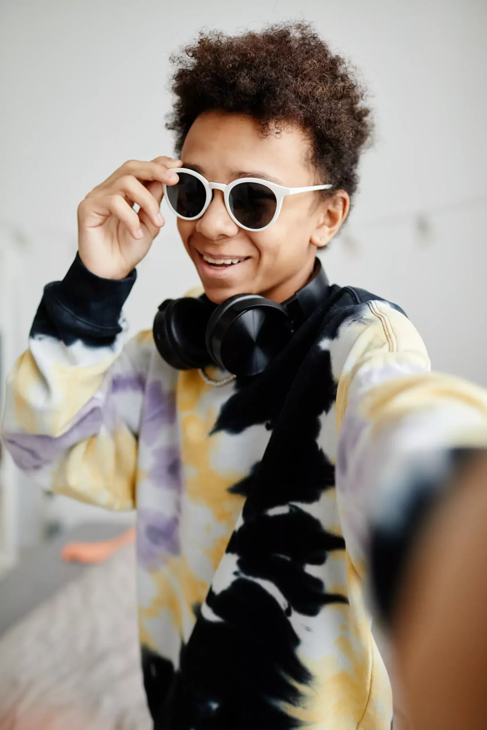 ADOBESTOCK_511228321 SCALED | Cekome Adolescent portant des lunettes de soleil blanches et un casque audio autour du cou, prenant un selfie