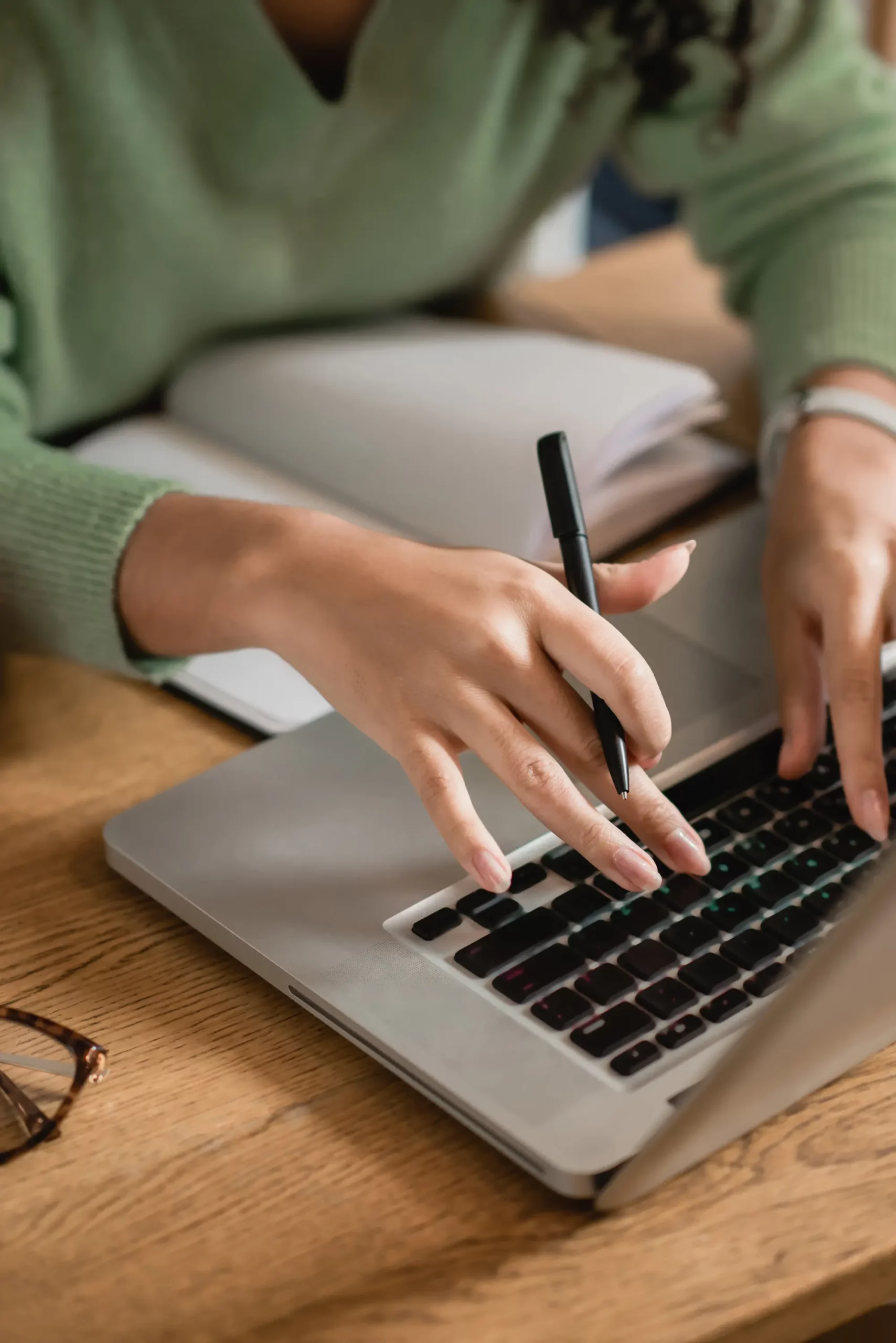 ADOBESTOCK_403229478 SCALED | Cekome Personne utilisant un ordinateur portable avec un stylo à la main, cahier ouvert en arrière-plan