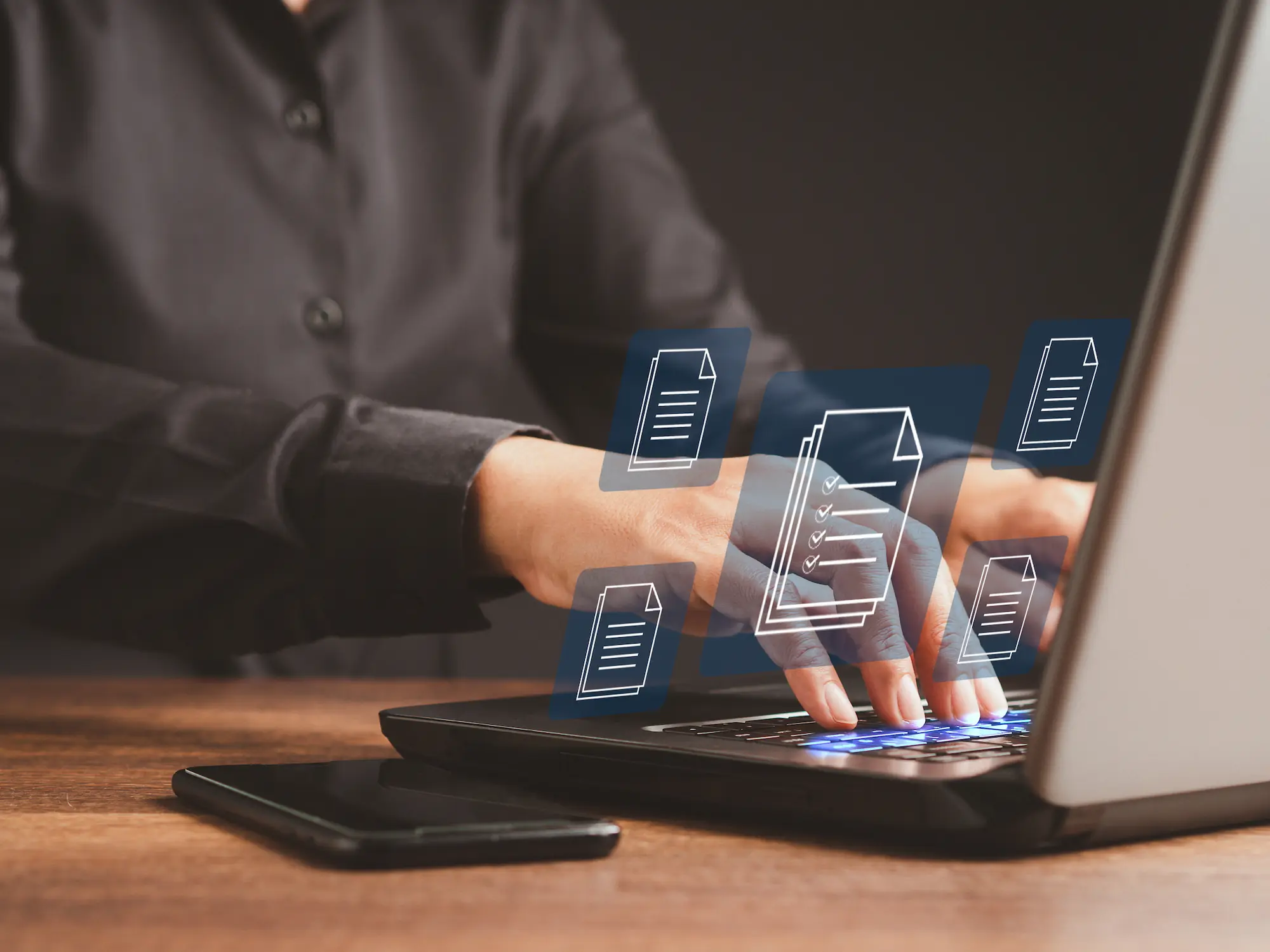 Personne en chemise noire tapant sur un ordinateur portable avec des icônes de documents holographiques