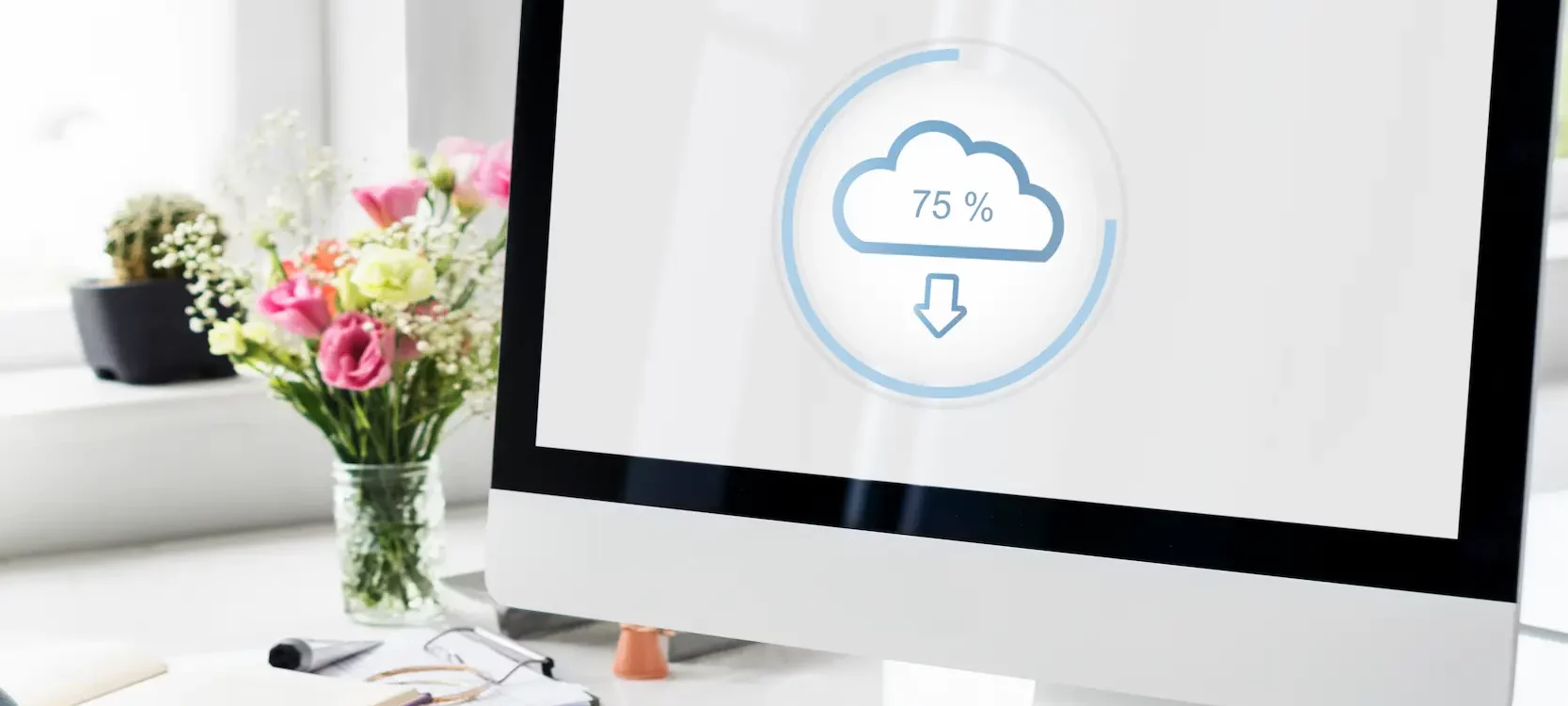 Ordinateur affichant un t&eacute;l&eacute;chargement cloud &agrave; 75 % dans un environnement de bureau lumineux avec des fleurs et une tasse de th&eacute;