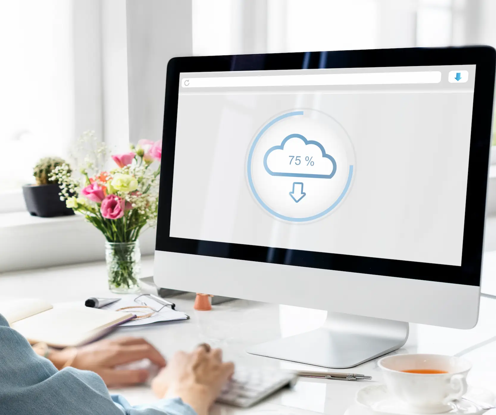 Ordinateur affichant un téléchargement cloud à 75 % dans un environnement de bureau lumineux avec des fleurs et une tasse de thé