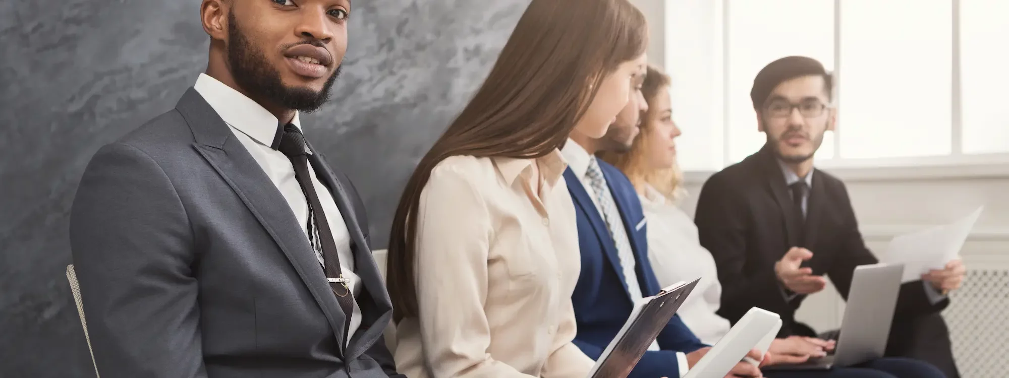 Candidats en costume attendant une entrevue, assis en rangée avec des documents en main