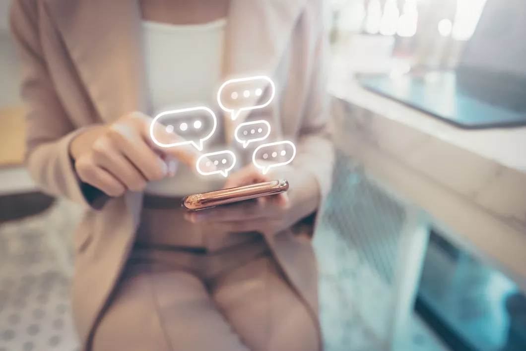 Femme en tailleur beige utilisant un smartphone avec des bulles de dialogue lumineuses flottantes.