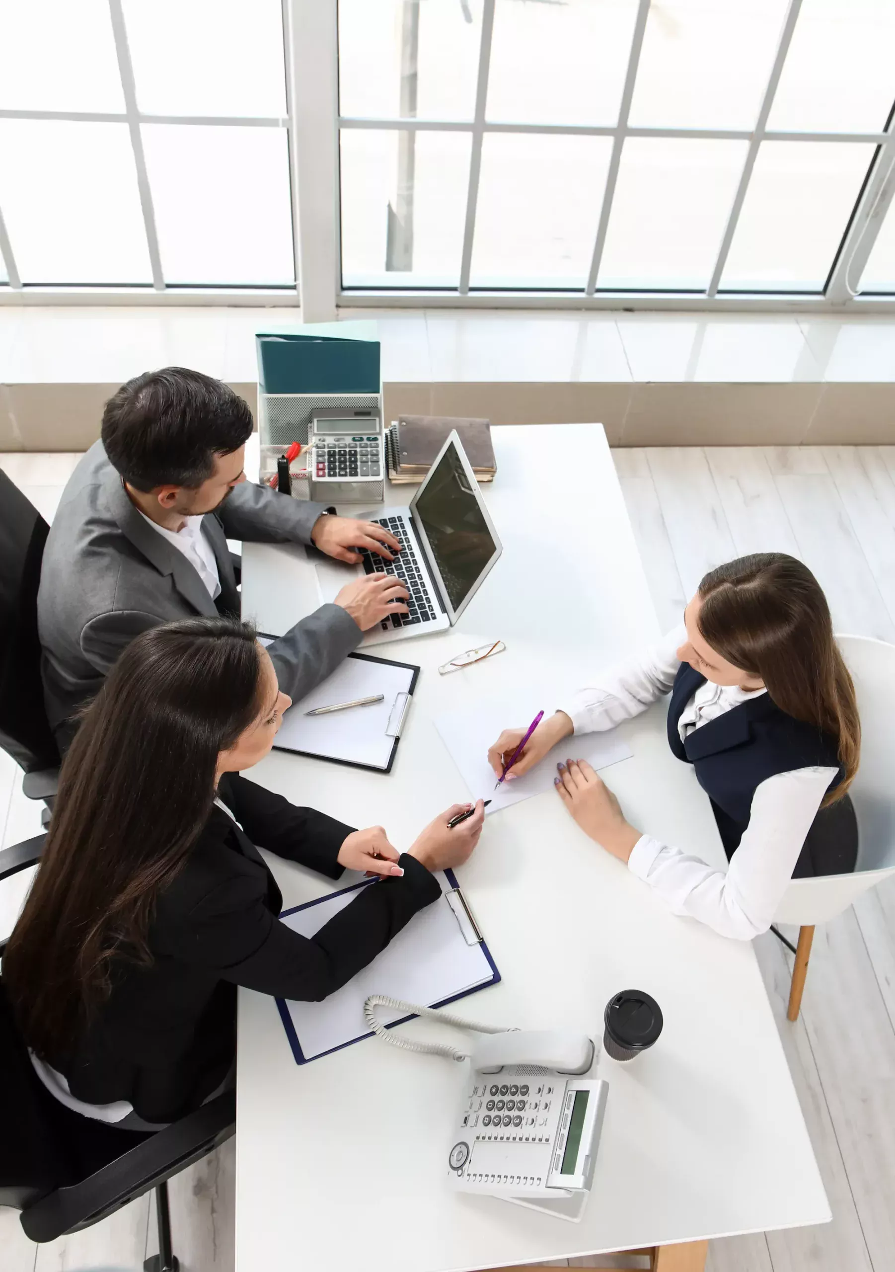 ADOBESTOCK_703593419 SCALED | Cekome Réunion de trois personnes autour d'une table dans un bureau moderne, une femme prenant des notes