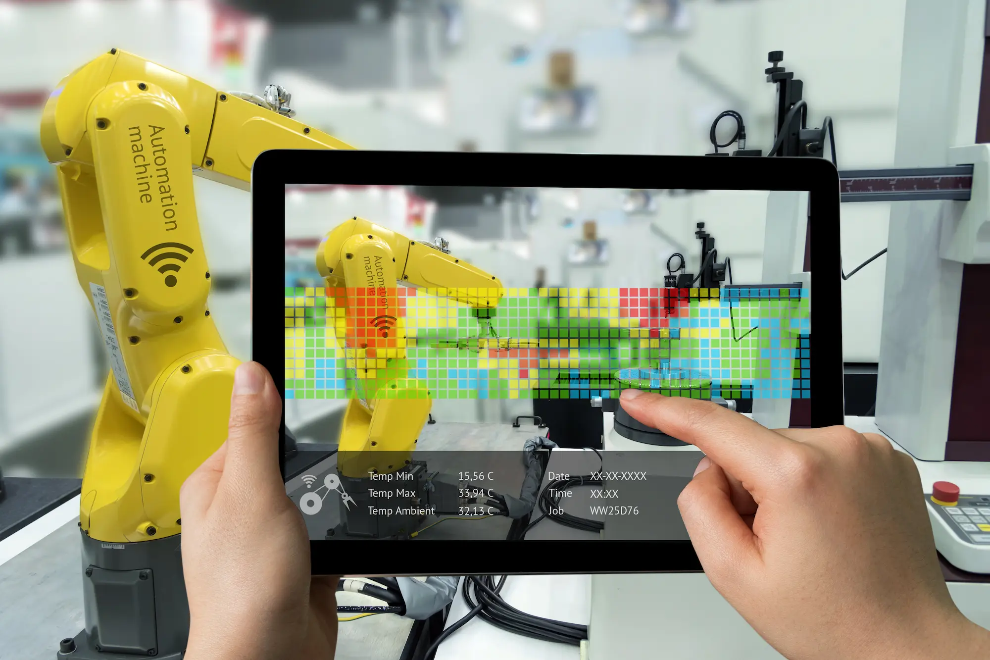 Main tenant une tablette affichant des données en réalité augmentée devant un bras robotisé jaune dans une usine automatisée