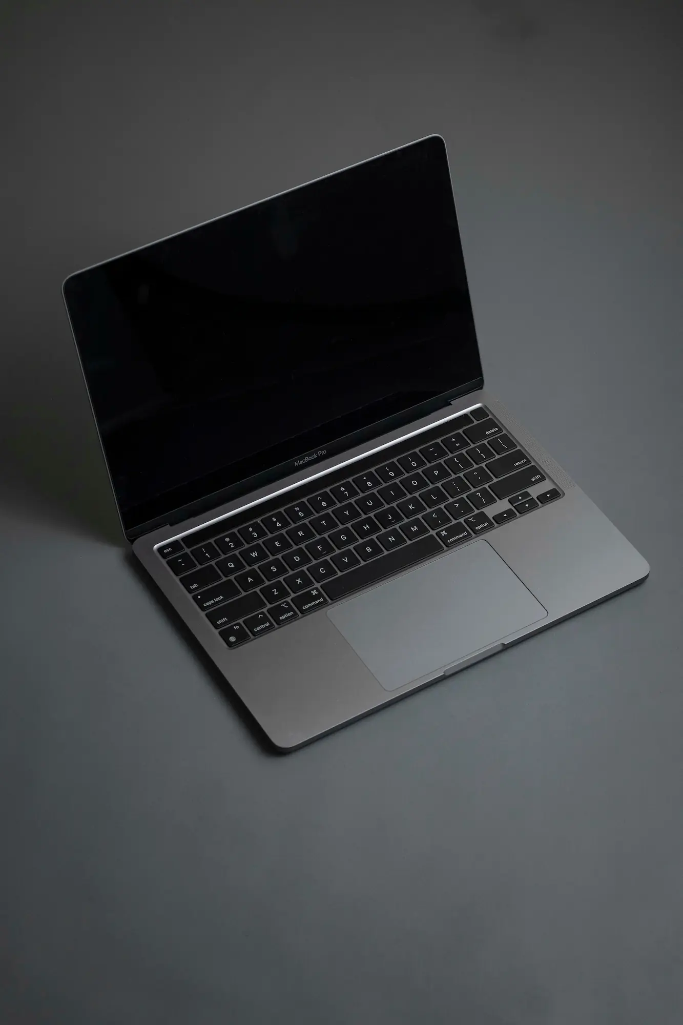 ADOBESTOCK_457144050 | Cekome Ordinateur portable MacBook Pro ouvert, posé sur une surface sombre avec un écran noir.