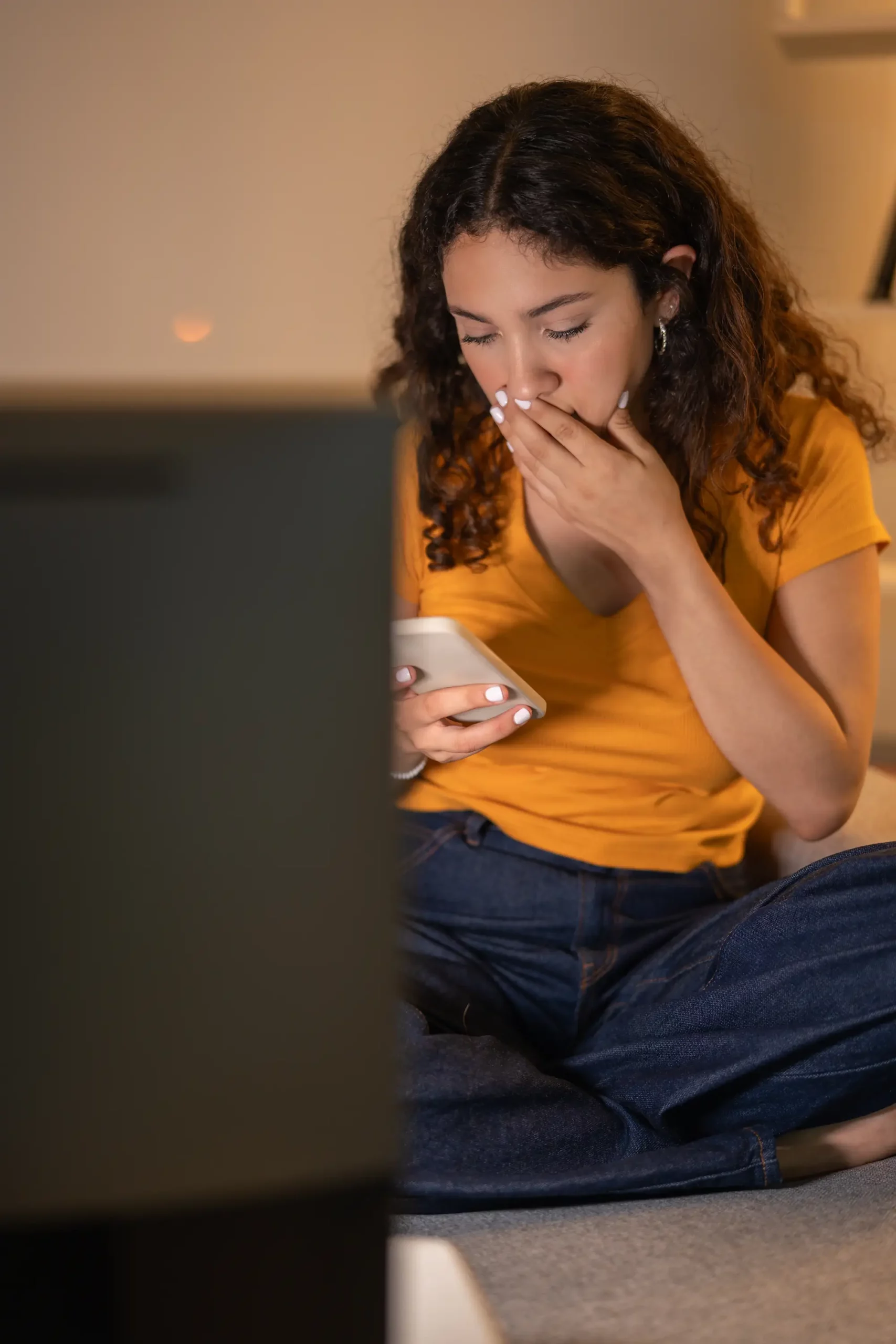 Femme assise, regardant son smartphone avec une expression de surprise