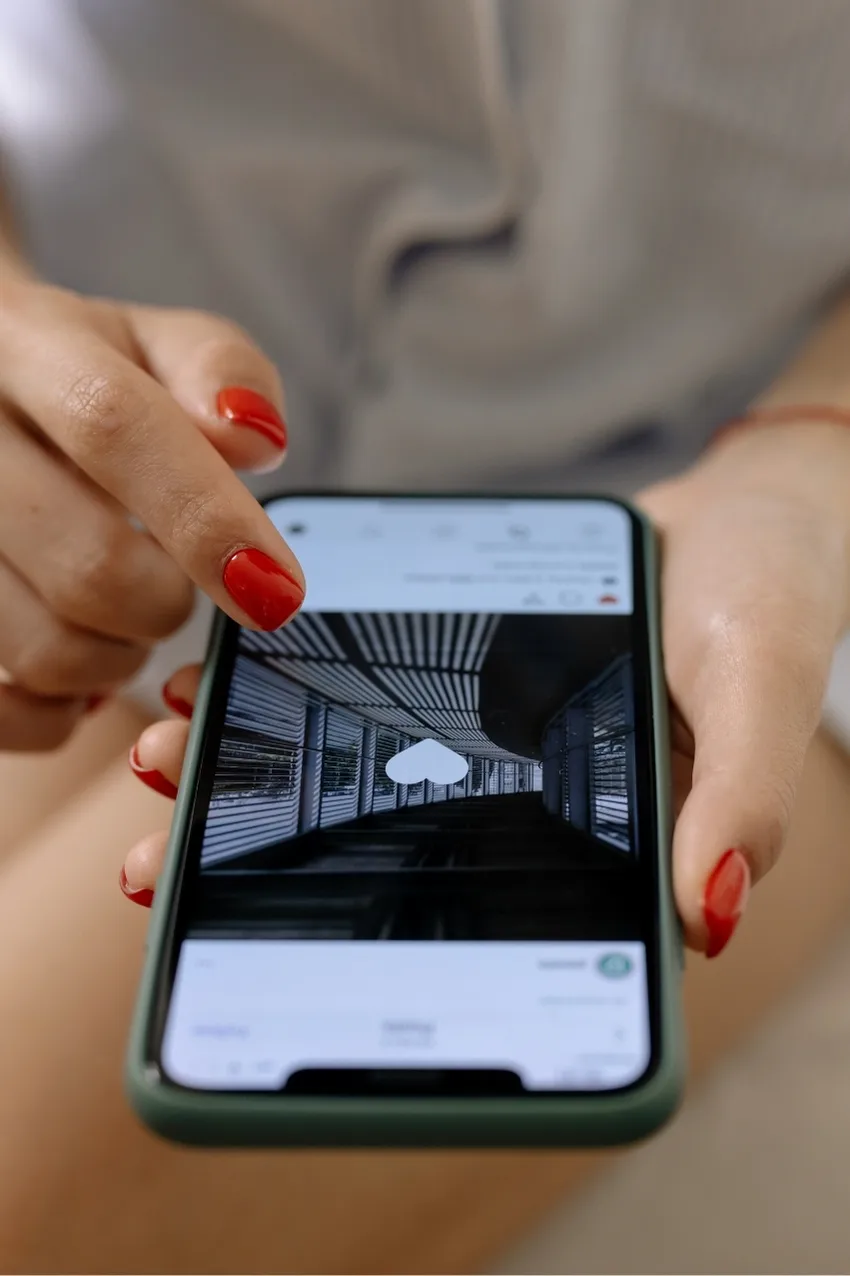 Gros plan sur une main avec des ongles rouges appuyant sur un like Instagram affiché sur l’écran d’un smartphone.