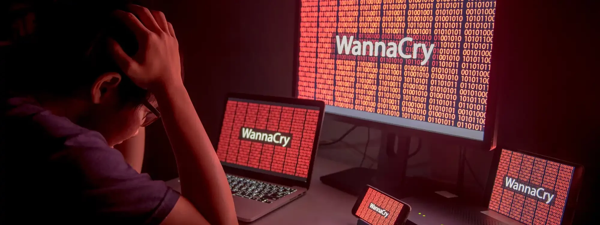 Personne désespérée devant plusieurs écrans affichant le ransomware WannaCry en rouge.