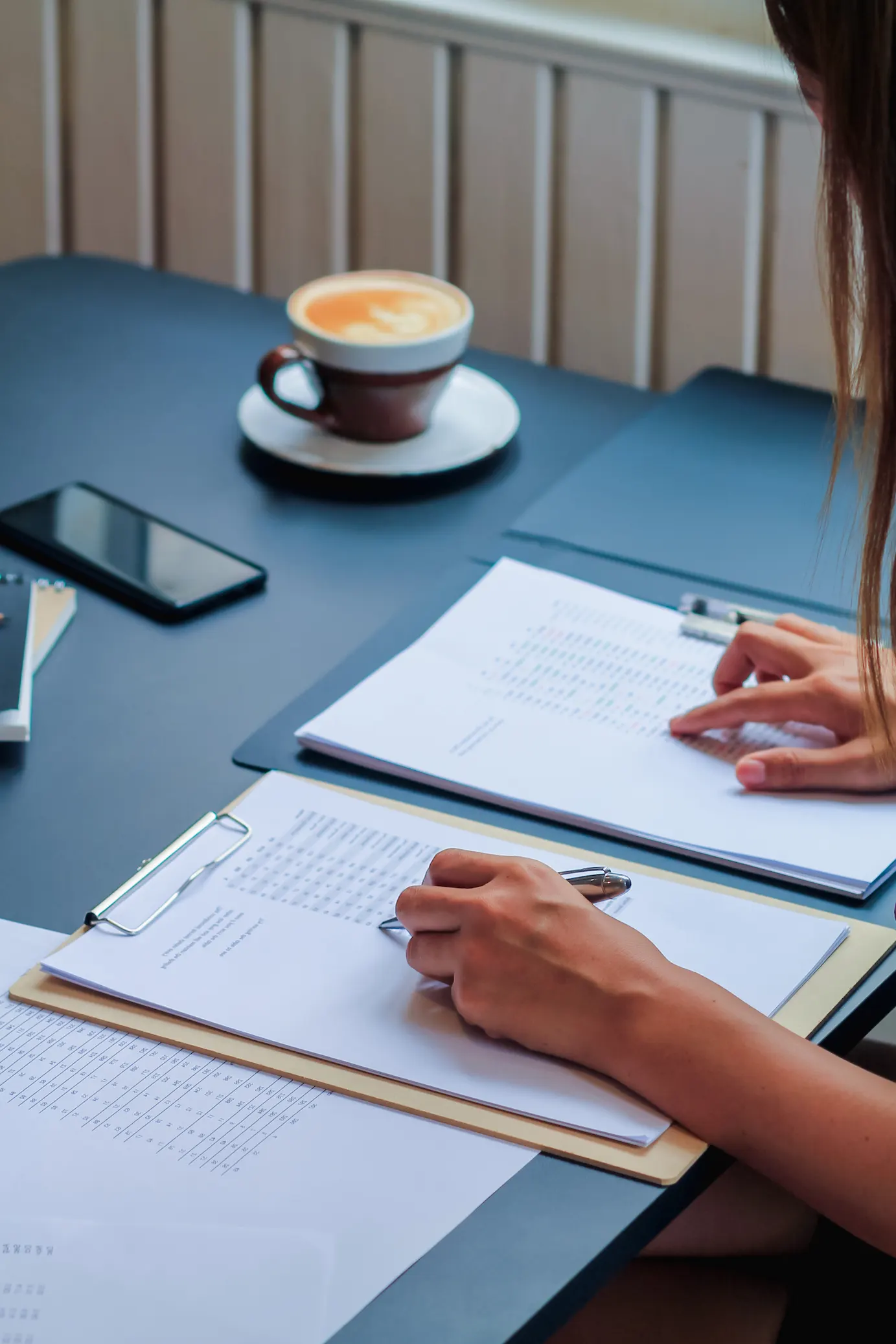 ADOBESTOCK_502441206 | Cekome Personne travaillant sur des documents avec un café et un smartphone sur une table