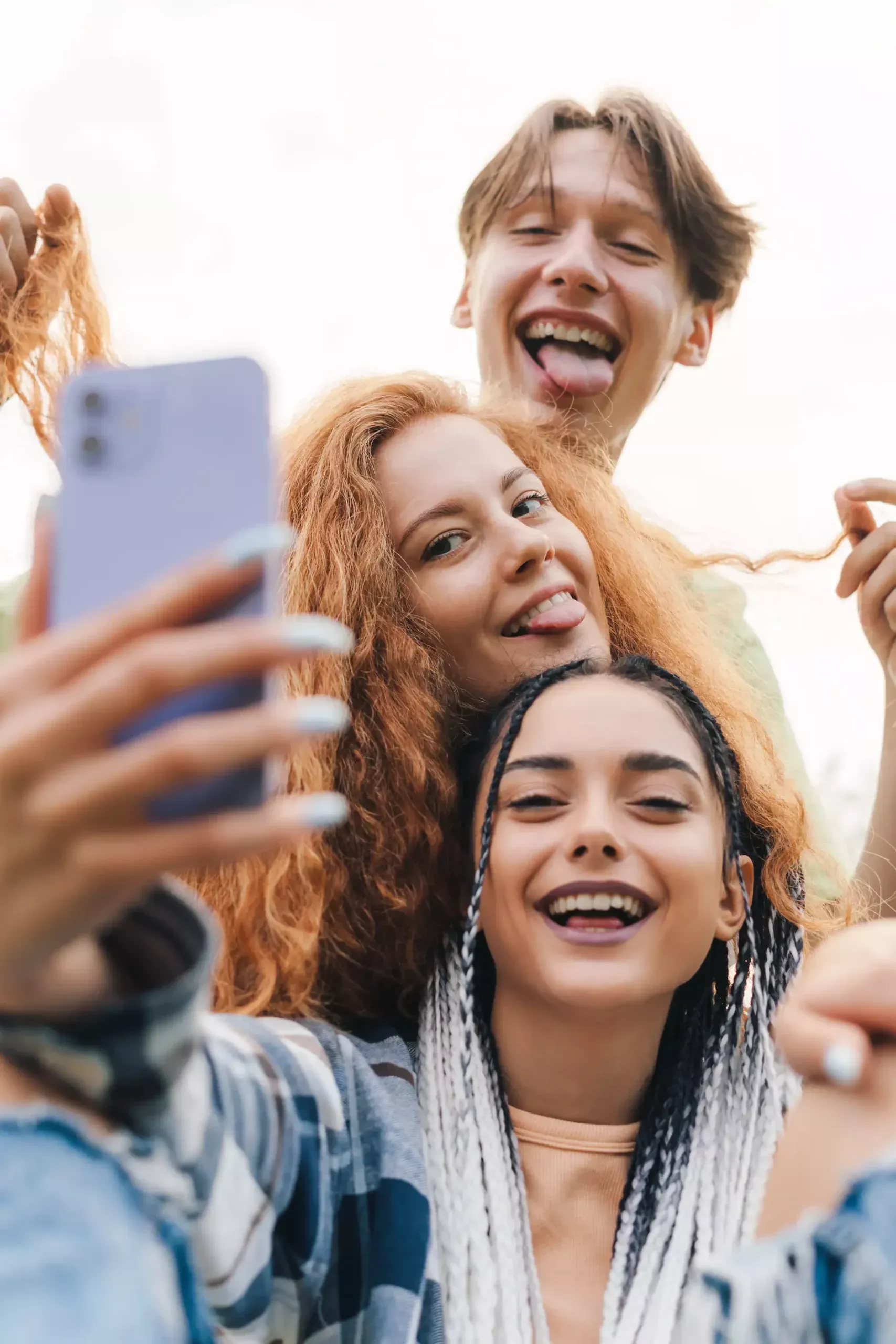 Trois amis souriants prenant un selfie ensemble en extérieur