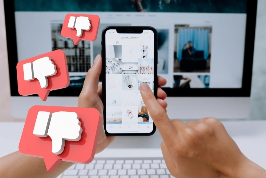Personne utilisant un smartphone avec des icônes de pouces baissés en 3D représentant des avis négatifs sur les réseaux sociaux.