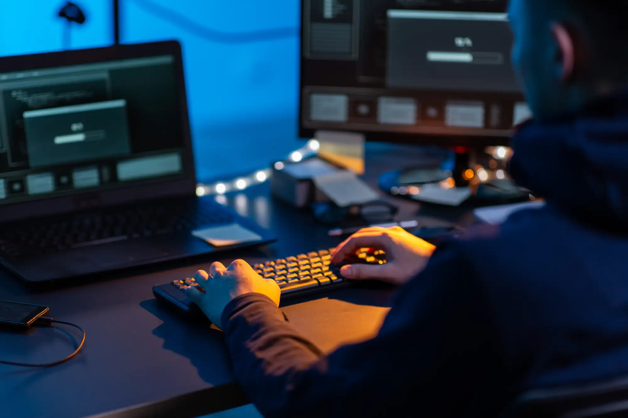 ADOBESTOCK_522472390 | Cekome Personne tapant sur un clavier d’ordinateur avec plusieurs écrans affichant des fenêtres de chargement et du code.