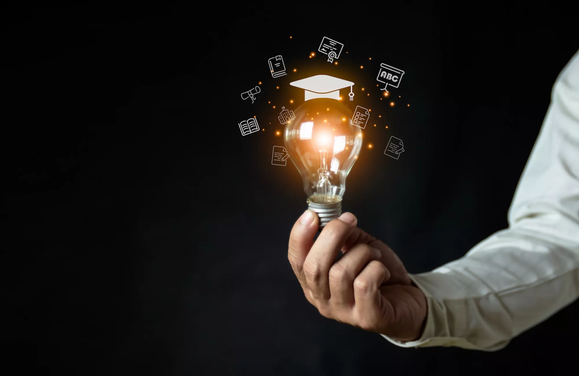 ADOBESTOCK_567649069 | Cekome Main tenant une ampoule allumée avec des icônes d'éducation flottant autour